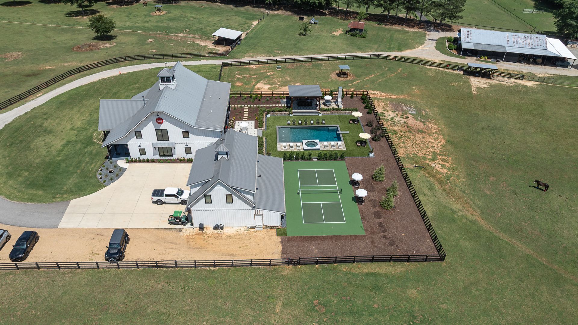 Aerial view of a house with a pool, tennis court, and large grassy yard.