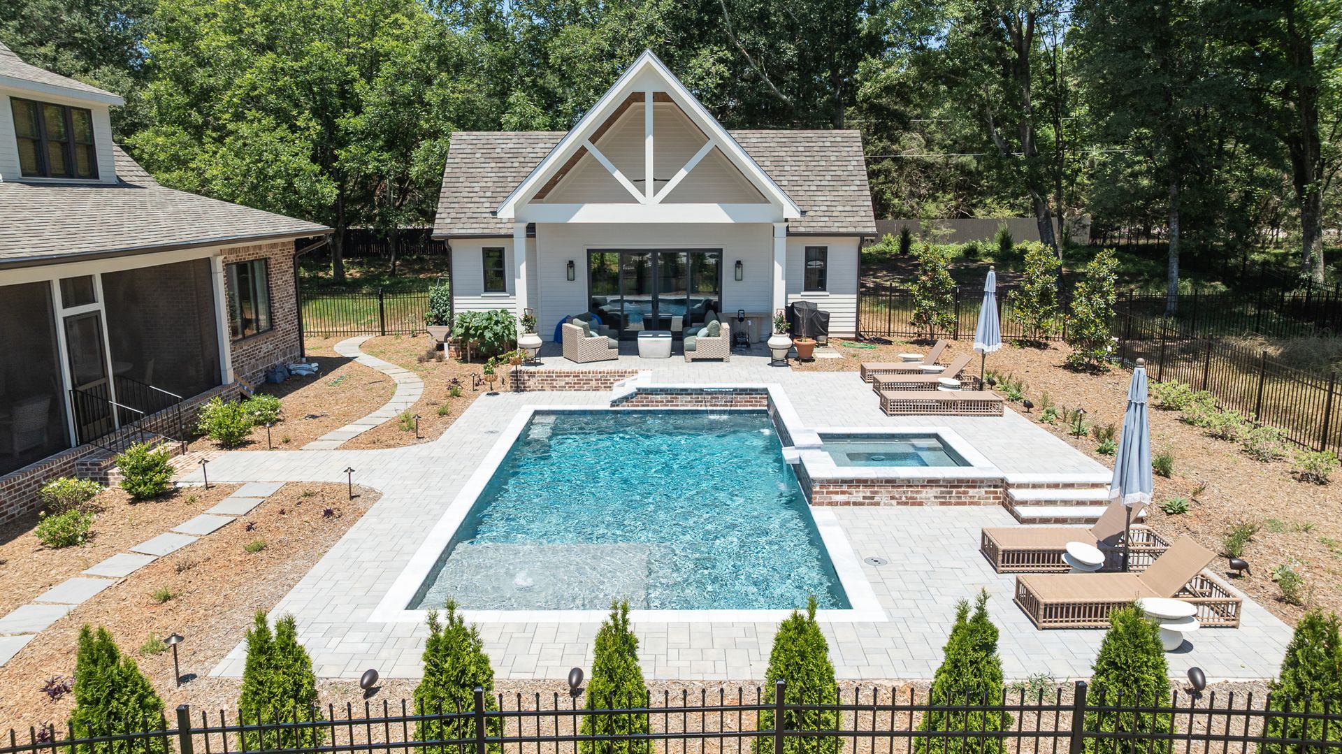 Backyard pool with lounge chairs, cabana, and landscaped patio beside a house