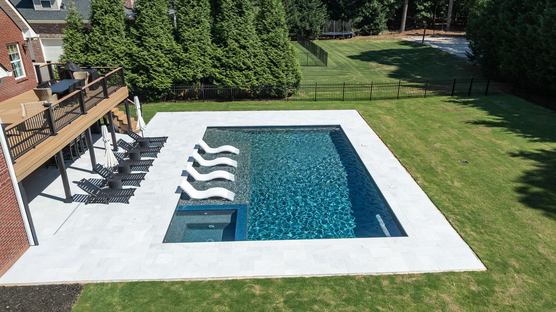 Backyard swimming pool with white deck, lawn, and deck chairs beside a house