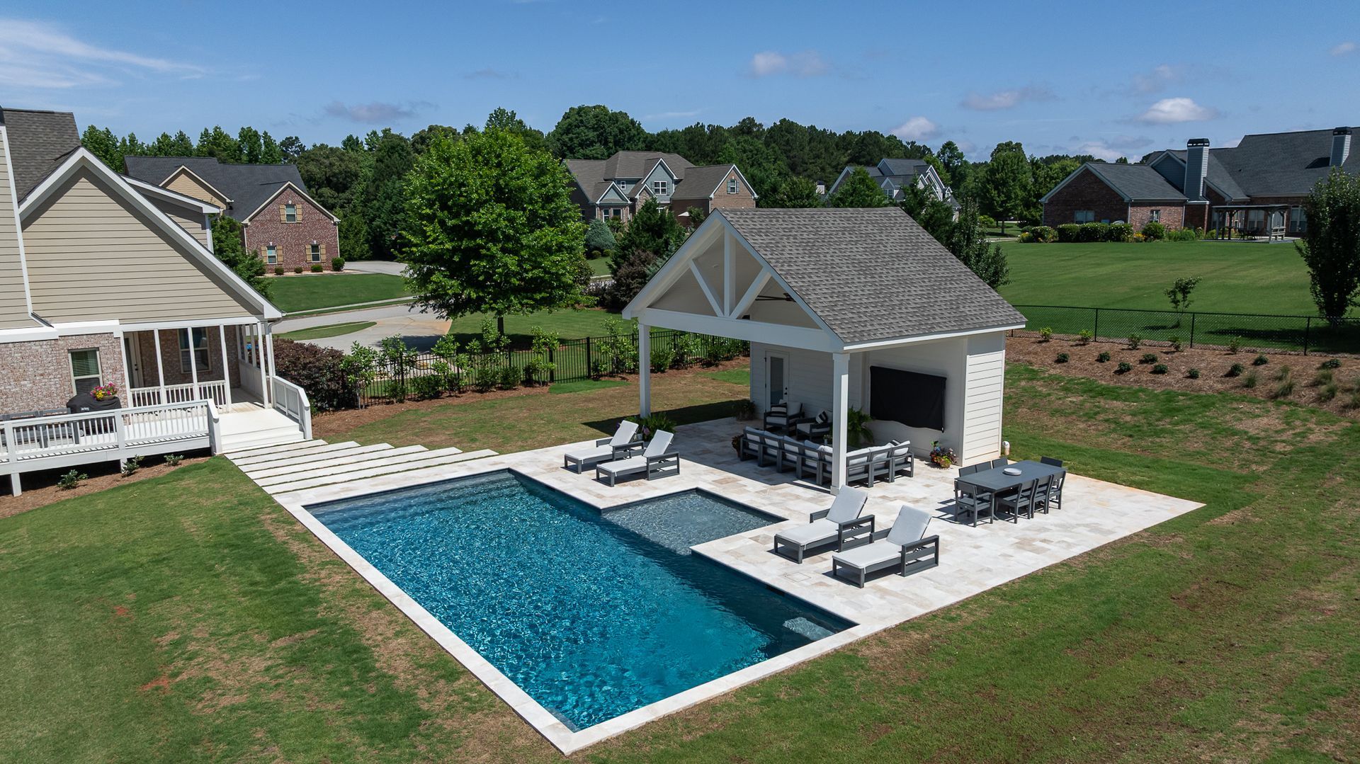 Backyard with rectangular pool, white patio cabana, lounge chairs, and green lawn in a suburban neighborhood