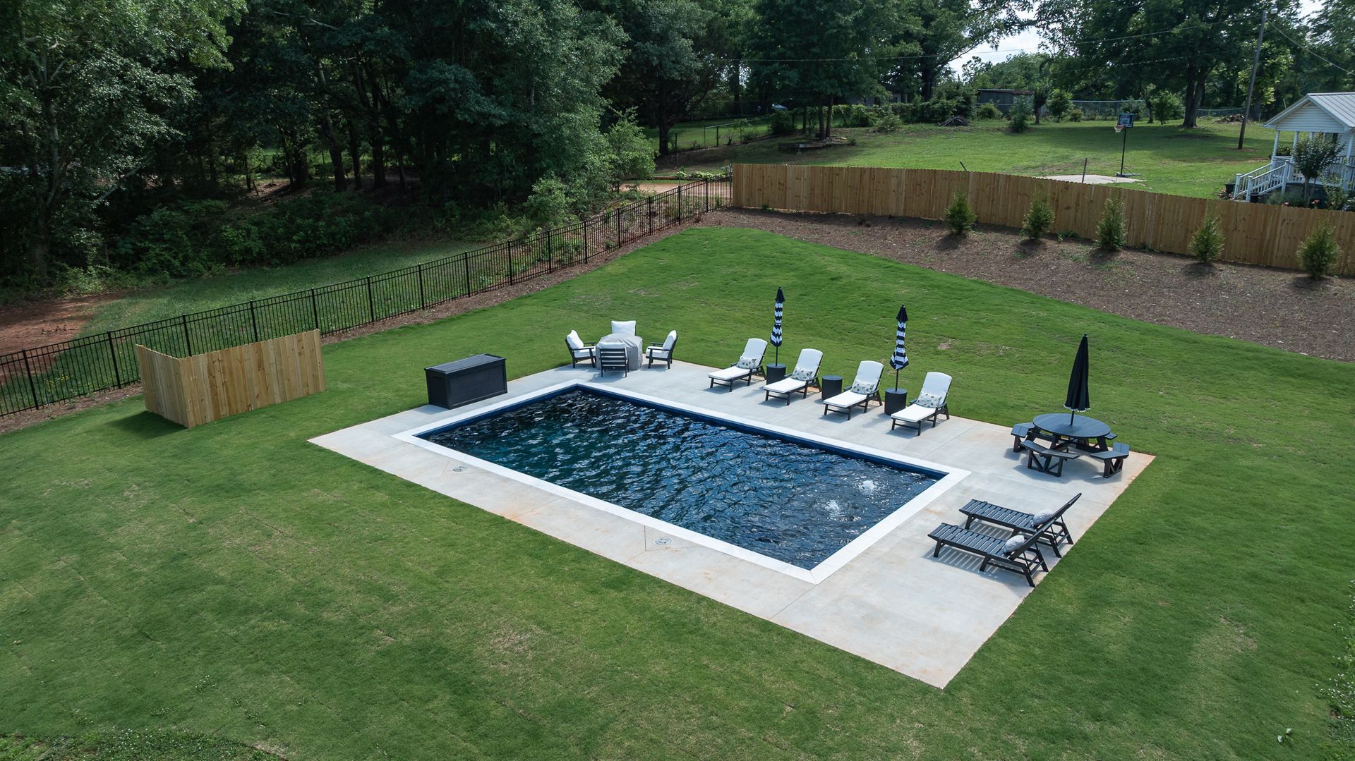 Backyard with a rectangular swimming pool, lounge chairs, and a seating area on a concrete patio