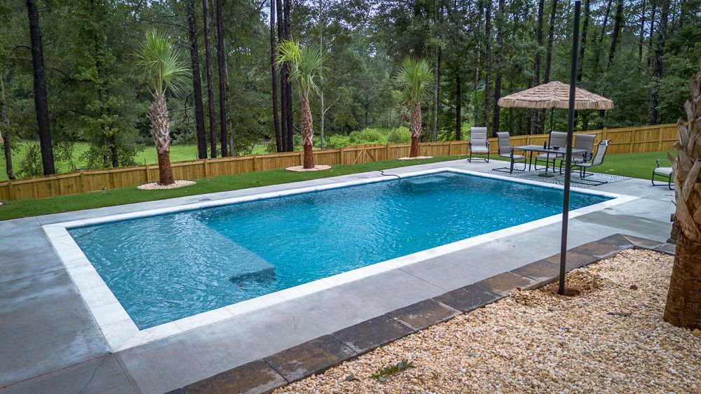 Backyard pool with blue water, concrete surround, and lounge area with a table and chairs.