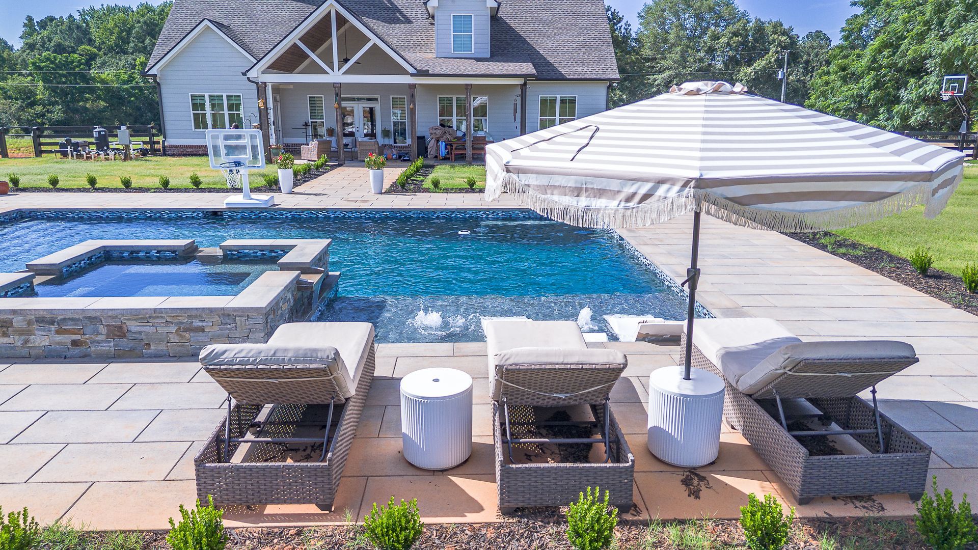 Poolside scene: Lounge chairs with umbrella, pool, and house in background.
