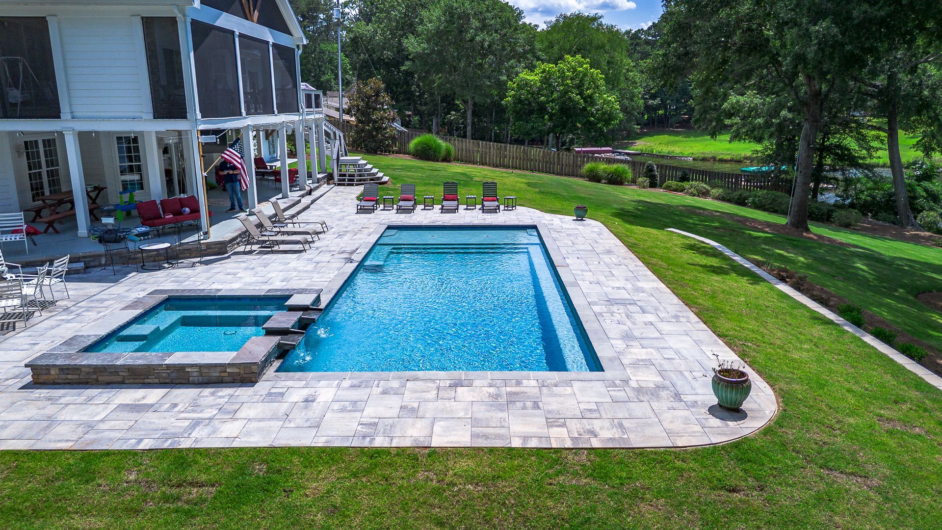 Outdoor pool and spa next to a large house on a grassy hillside.