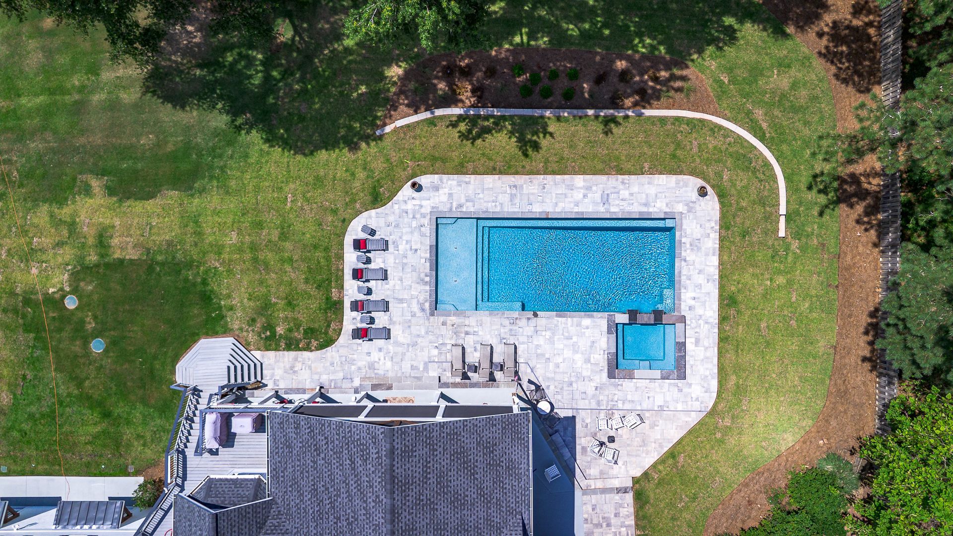 Overhead view of a backyard pool with a tanning deck, lawn, and part of a house.