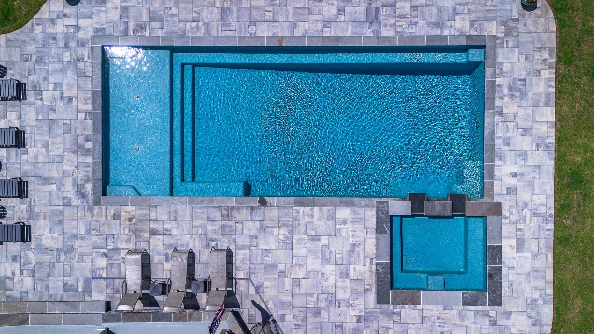 Overhead view of rectangular pool and spa, blue water, gray stone surround, and green grass.