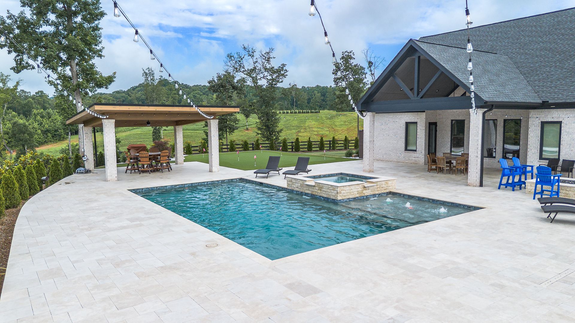 Outdoor pool area with pool, hot tub, patio, and building with mountain backdrop.