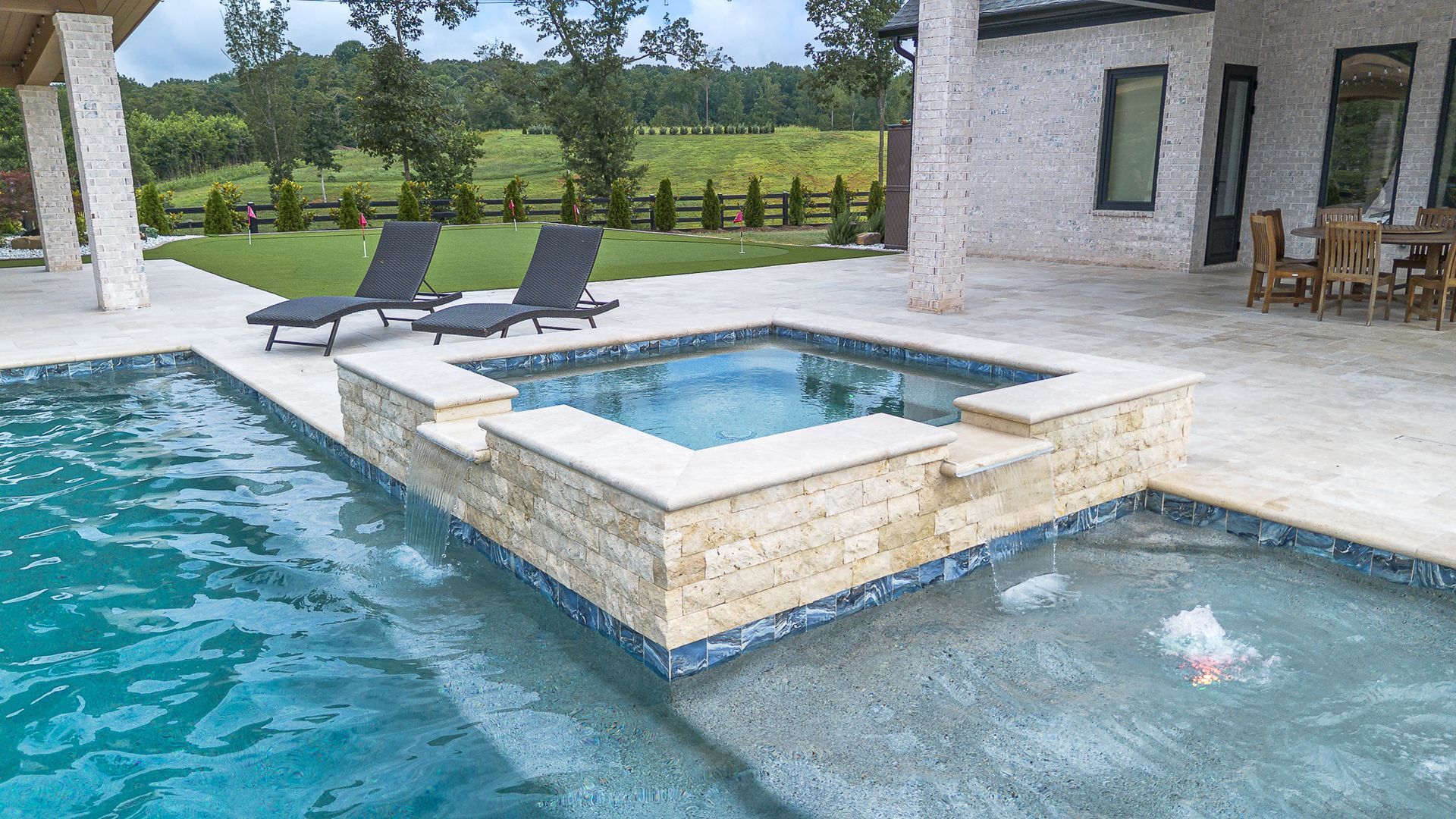 A luxurious pool area with a hot tub, lounge chairs, and a view of a green field.