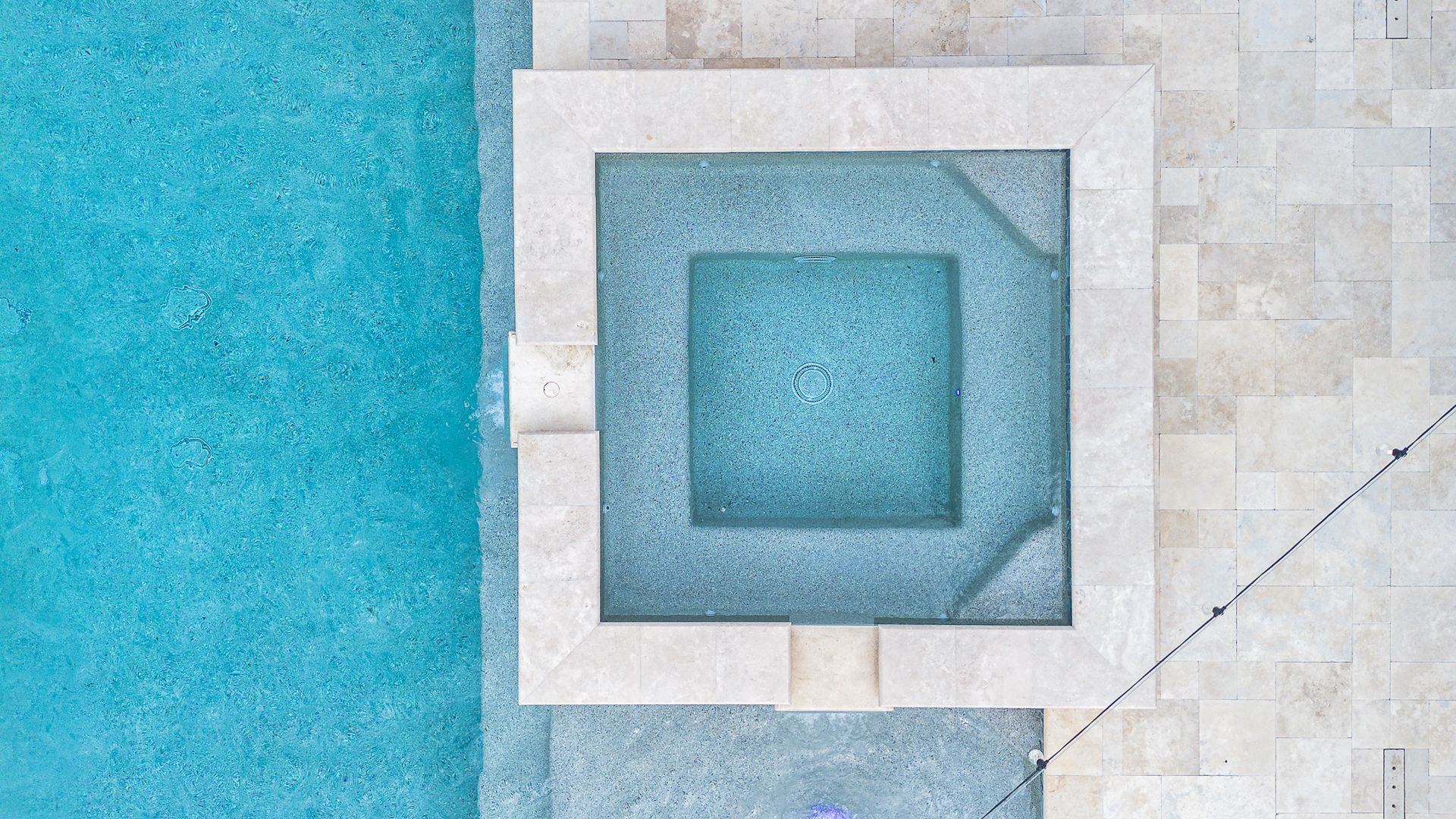 Overhead view of a swimming pool and spa with blue water, beige stone surround.