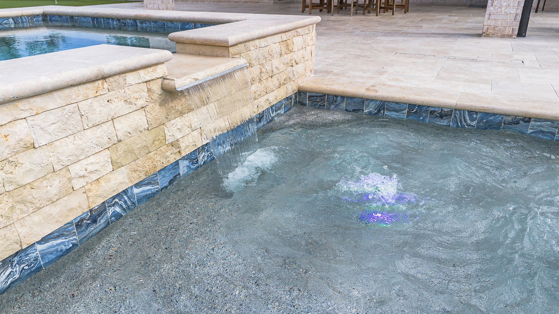 Hot tub with blue tile and stone wall, water bubbling.