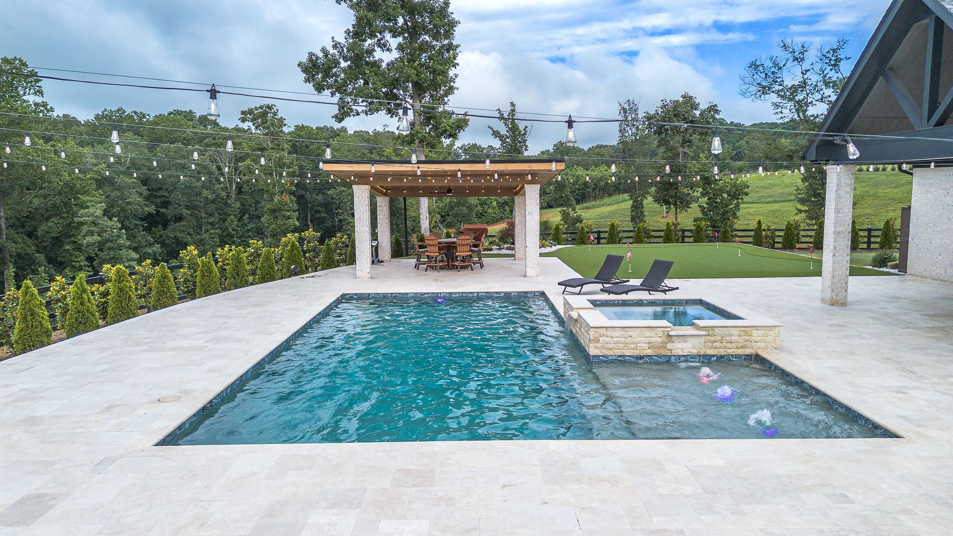 Pool with patio, pergola, and spa overlooking a lush green landscape.