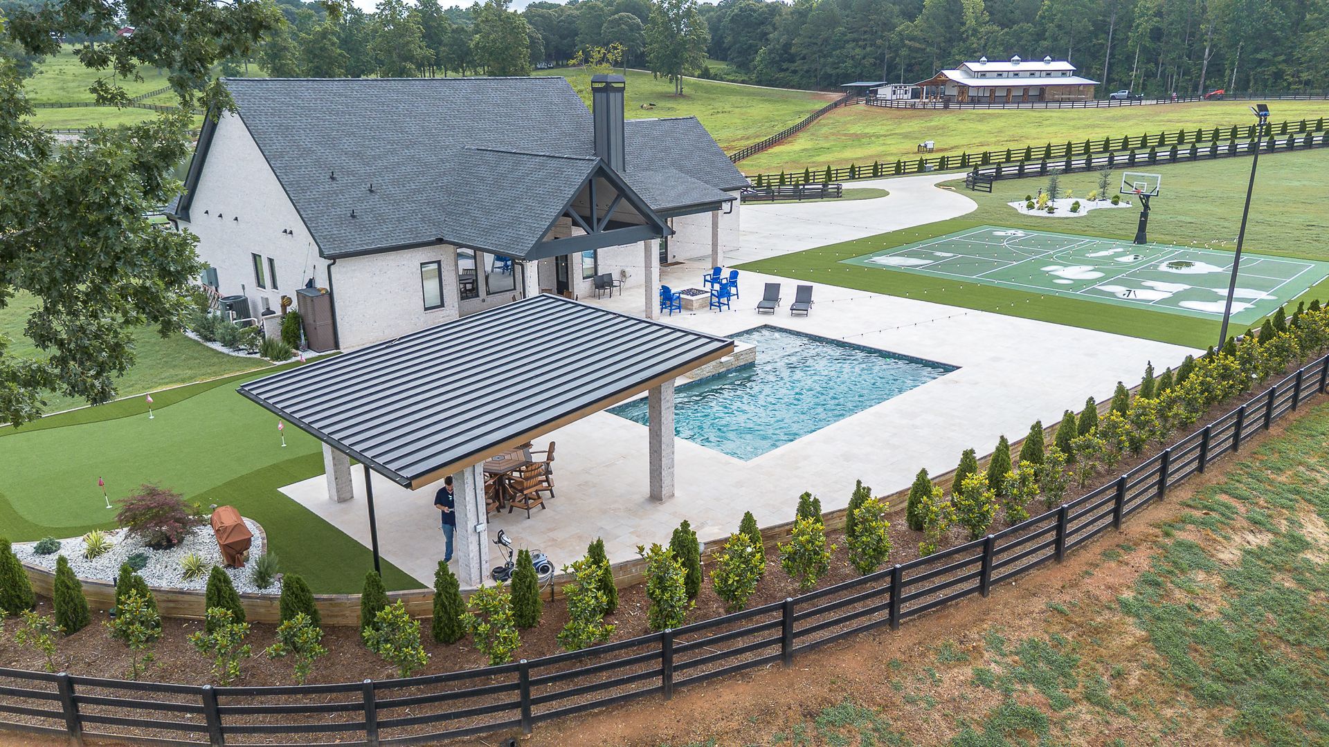 White house with pool, patio, and green turf area, behind a black fence.