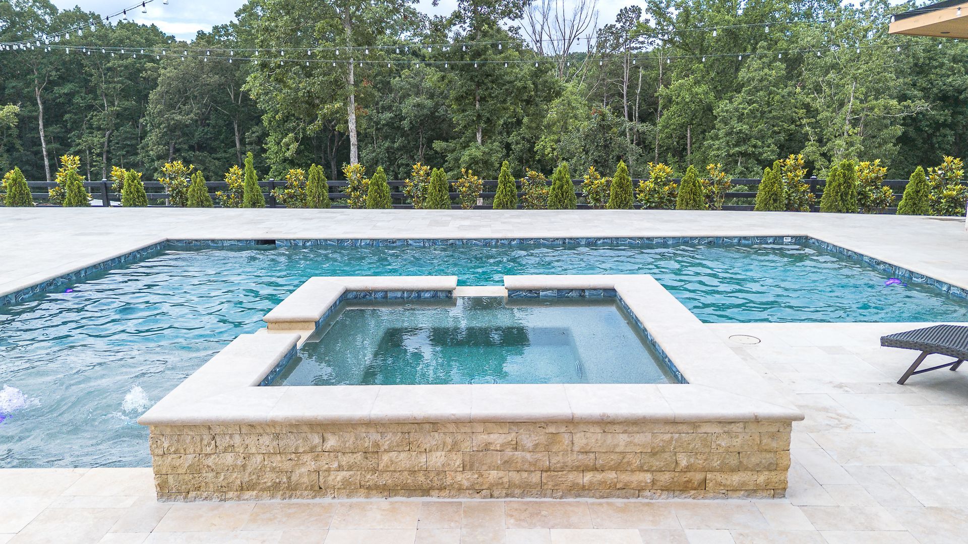 Pool and spa in a backyard setting, with a forest backdrop.