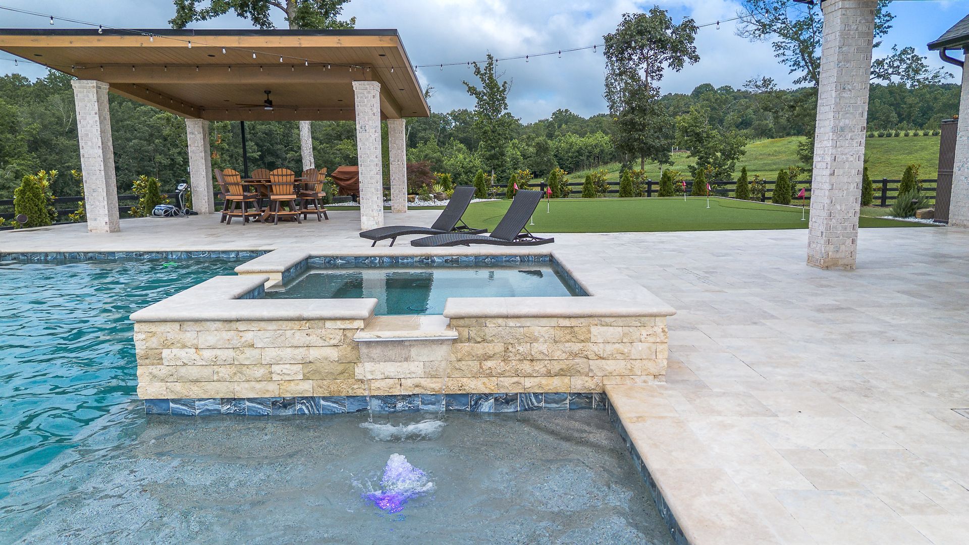 Swimming pool with a hot tub, patio, and a covered dining area in a lush backyard setting.