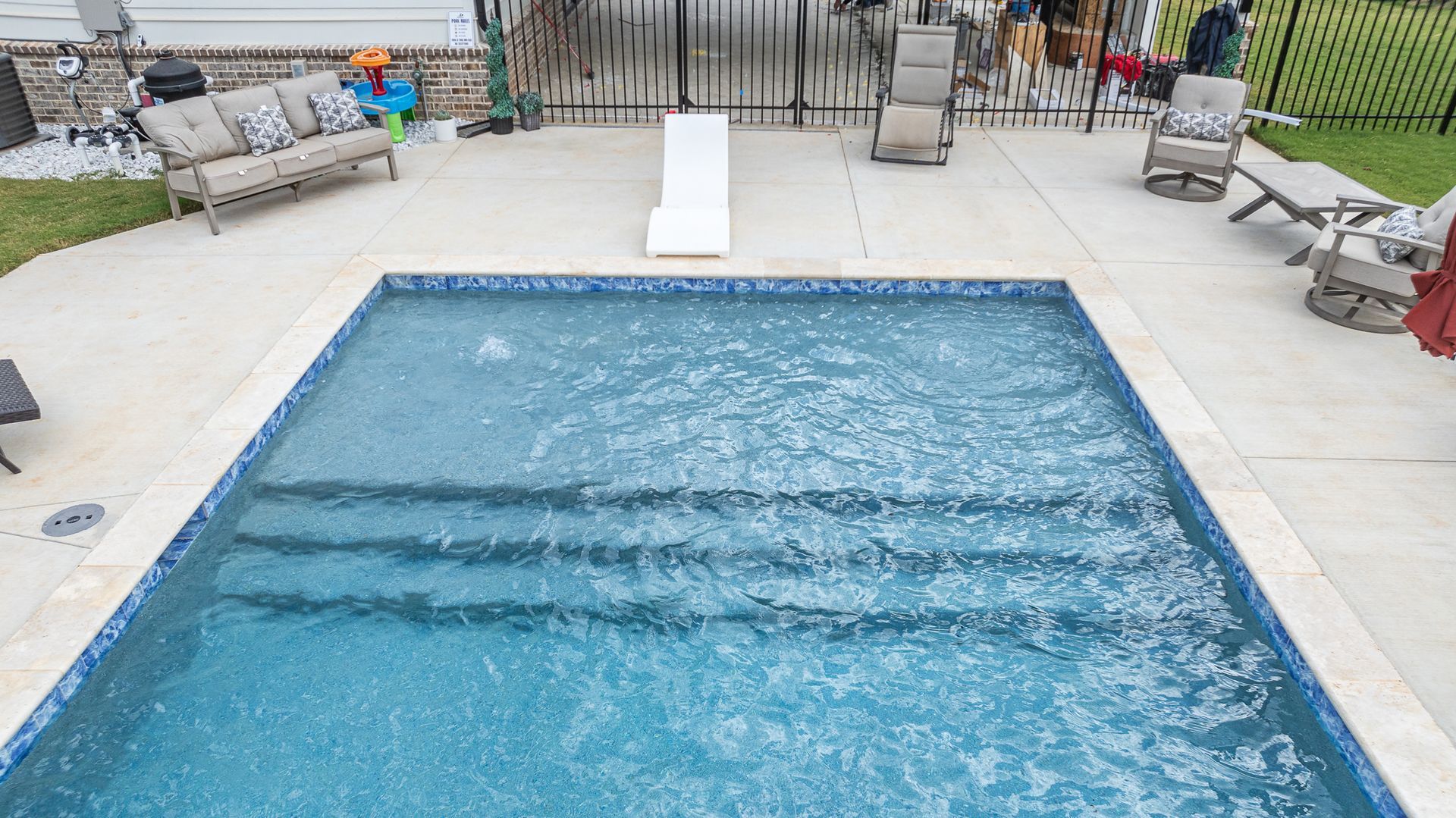 A large swimming pool surrounded by chairs and a couch in a backyard.
