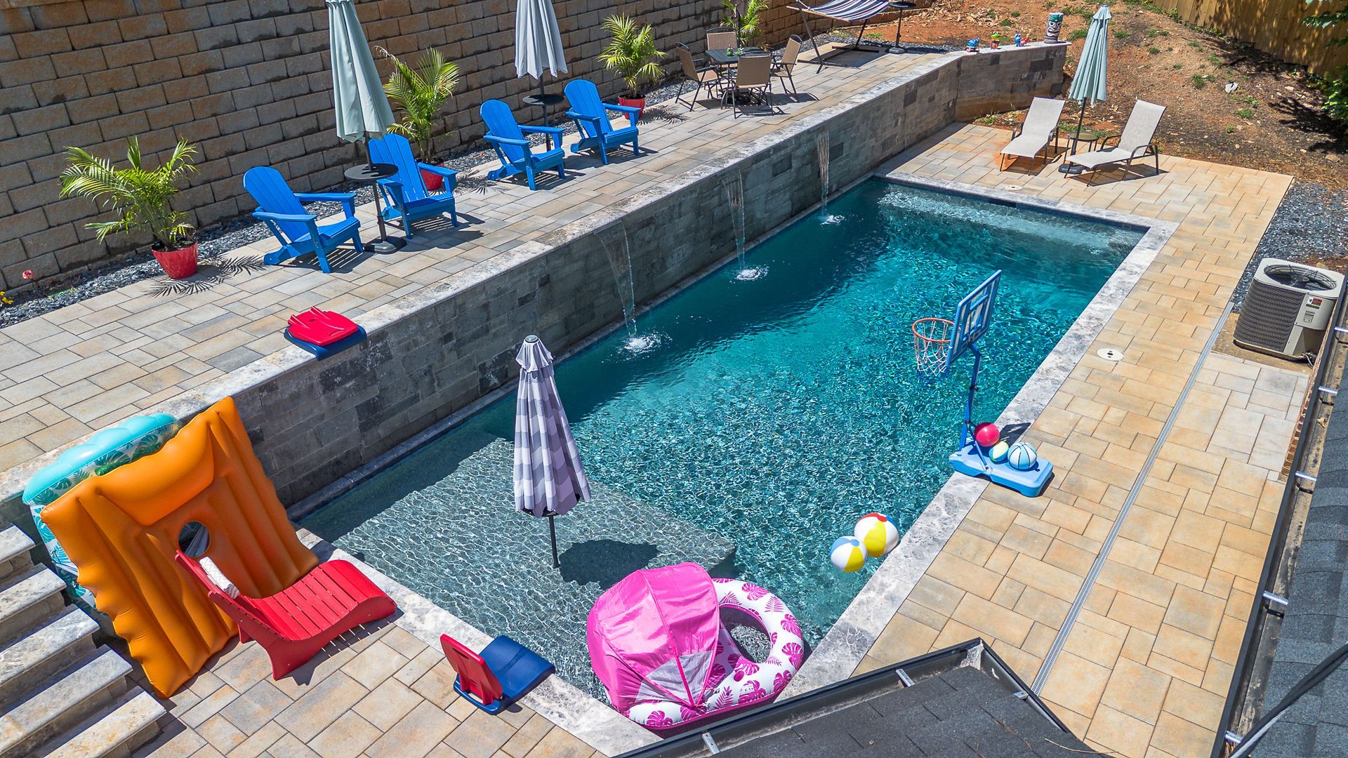 Backyard pool with lounge chairs, umbrellas, and pool toys.