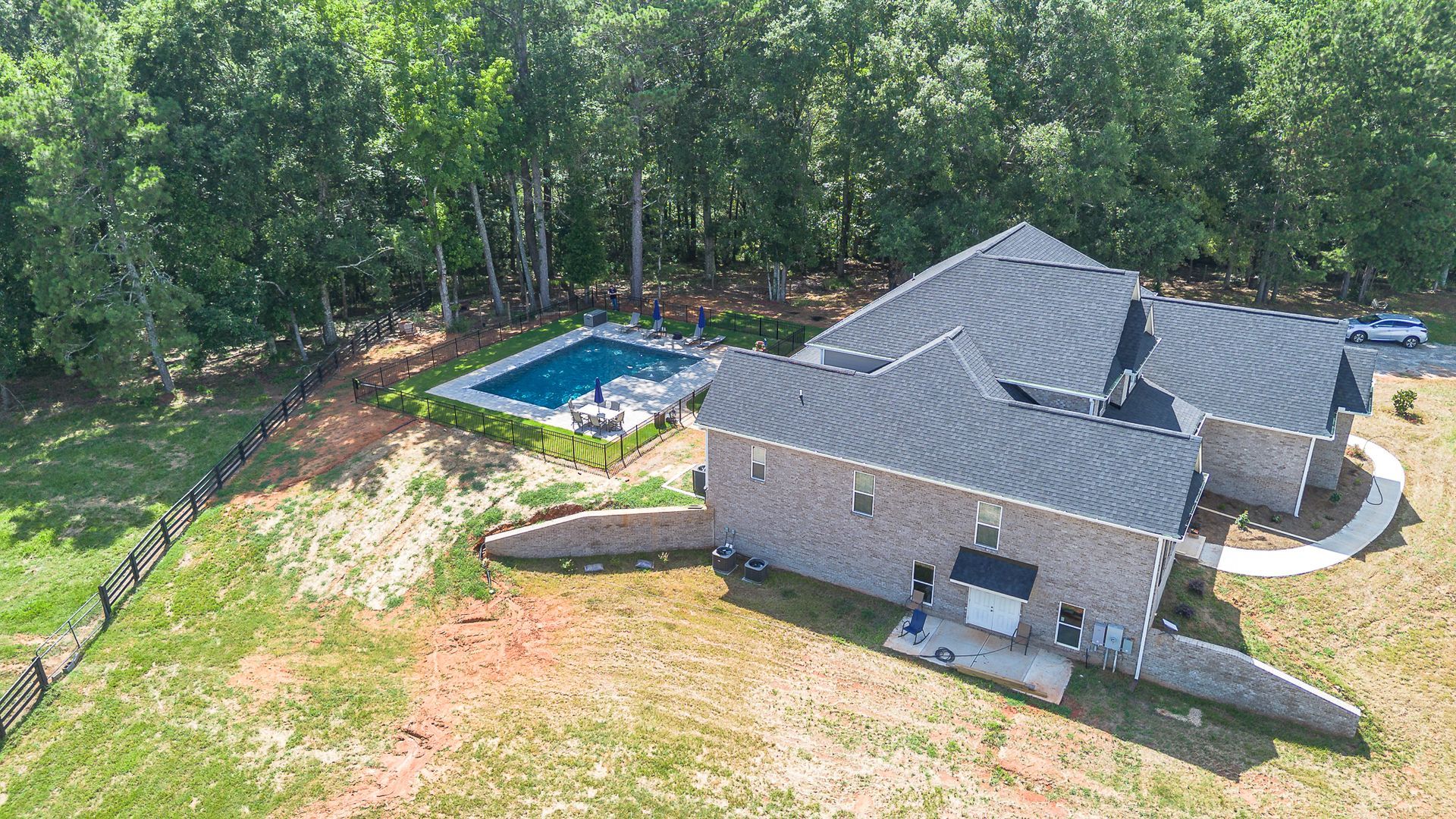 Aerial view of a brick house with a pool, surrounded by trees and grassy land.