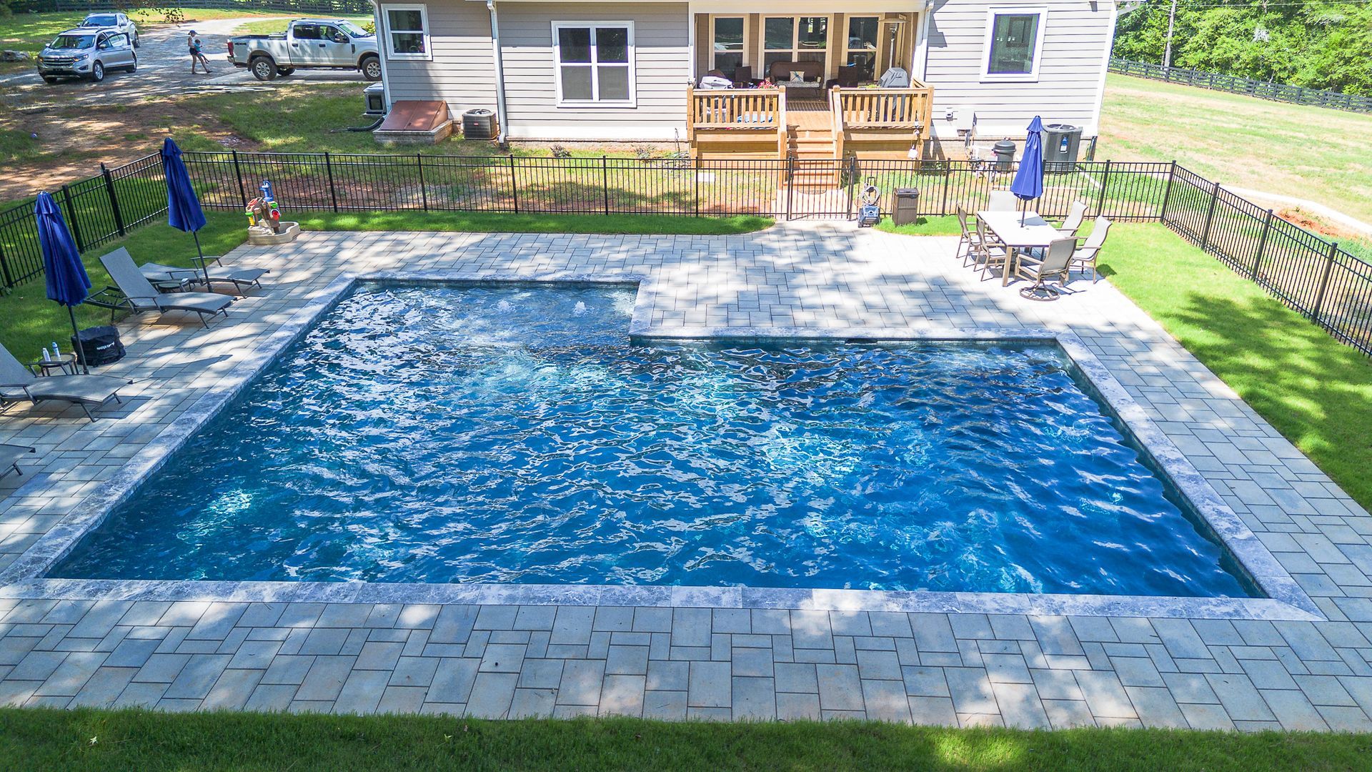Backyard pool with blue water, gray stone patio, and house in background.