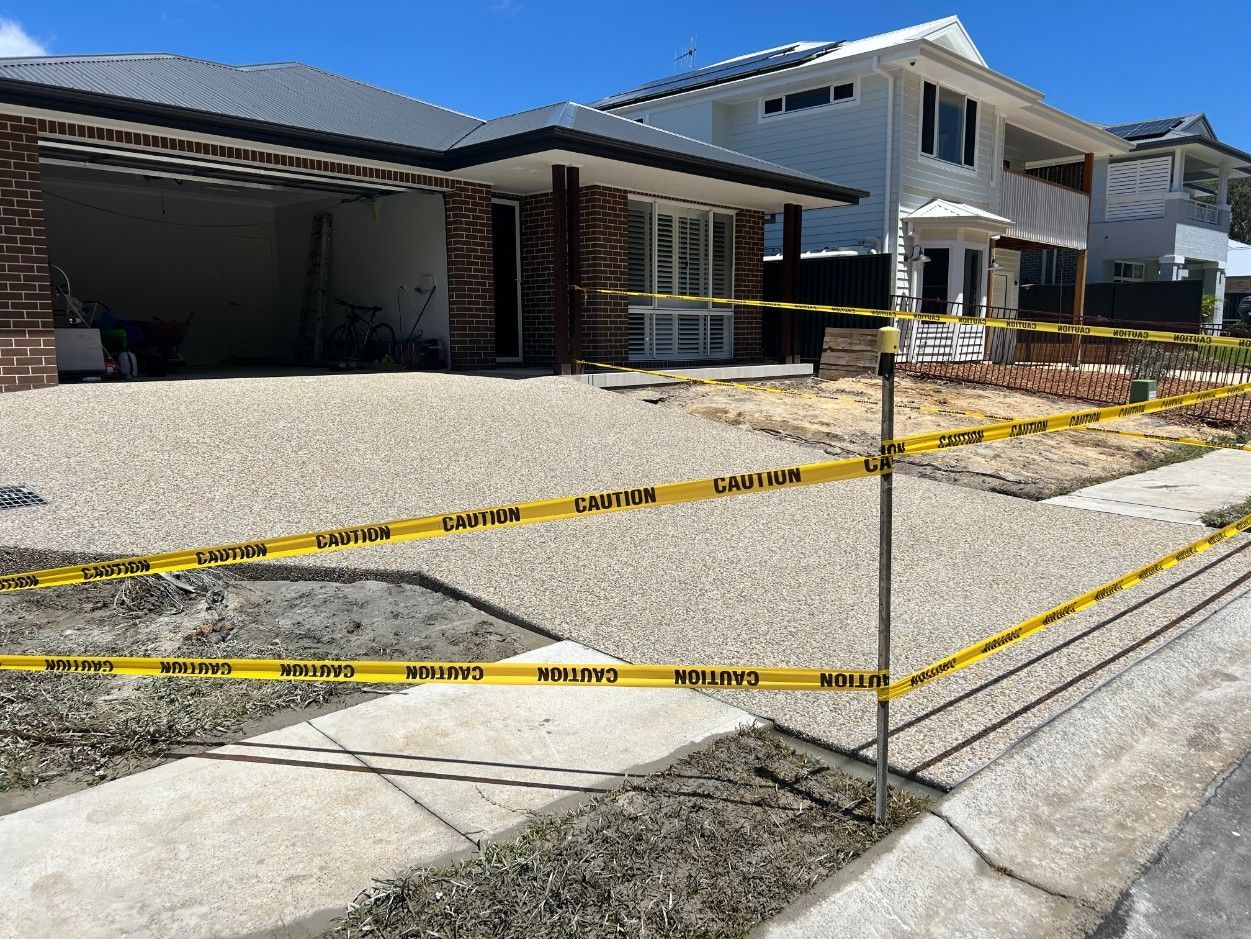 Caution Tape Blocks a Gravel Driveway in Front of A Modern House Under Construction — J’s Concreting & Carpentry in Kew, NSW