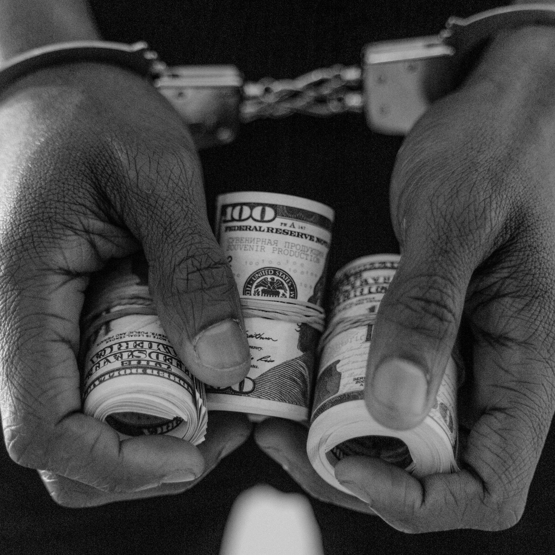 White Collar Crimes A man in handcuffs is holding two rolls of money in his hands.