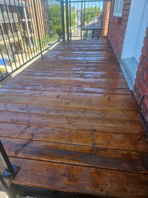 Balcon en bois humide avec rambarde noire, adossé à un mur de briques.