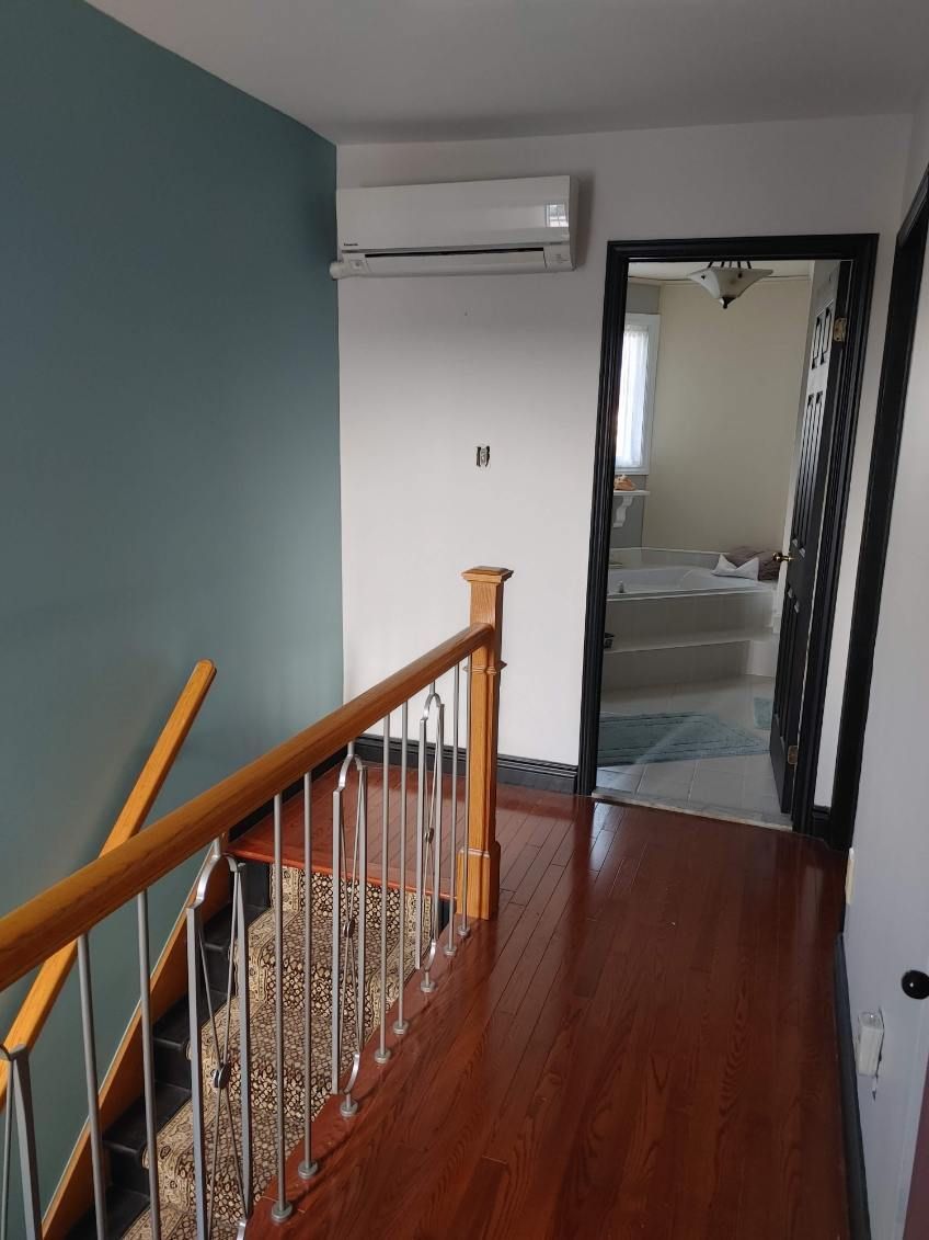 Couloir avec parquet, escalier et porte donnant sur une chambre. Murs bleu sarcelle et blancs, et climatisation réversible.