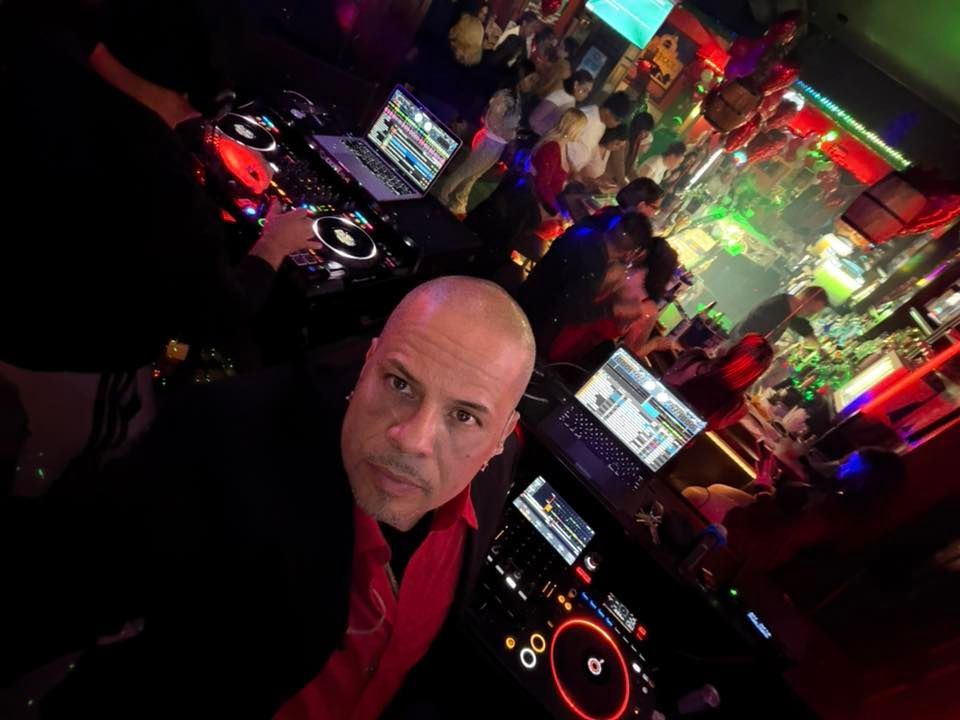 Man taking a selfie in a neon-lit nightclub with DJ equipment and screens in the background