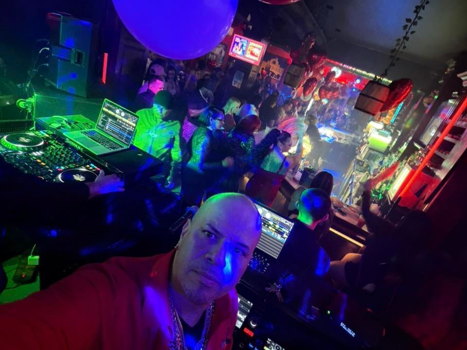 Crowded nightclub with neon lights, DJ equipment, and people dancing in the background