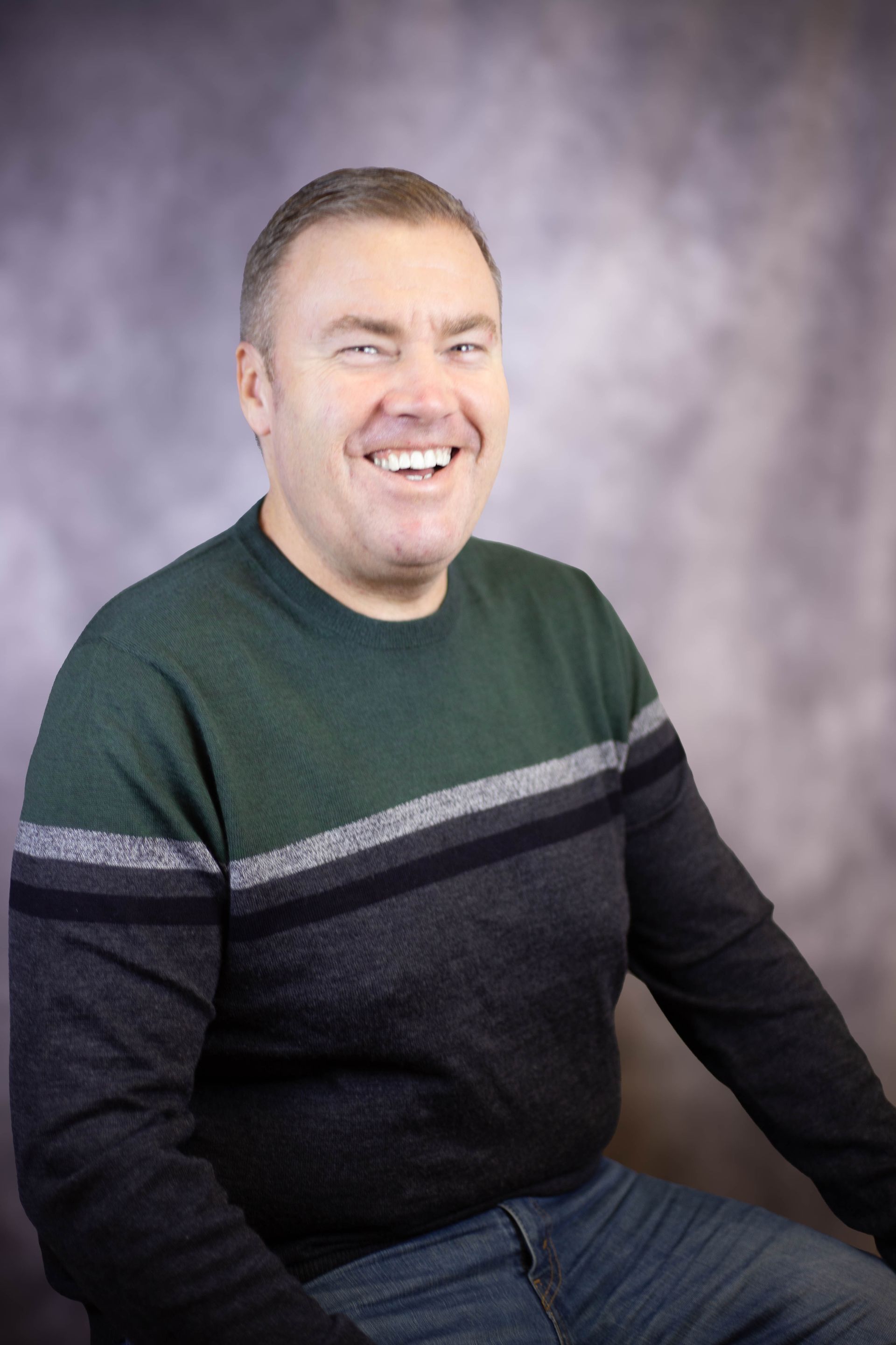 A man in a green and black sweater is smiling for the camera.