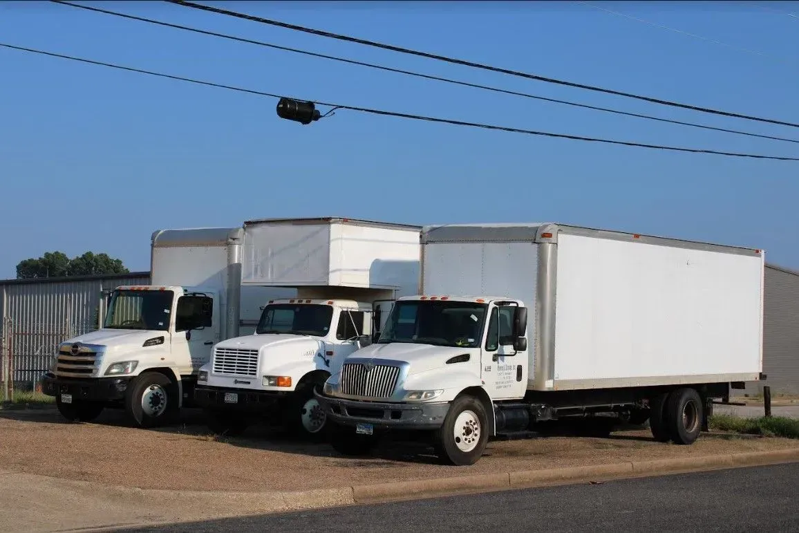Three white trucks are parked next to each other on the side of the road.