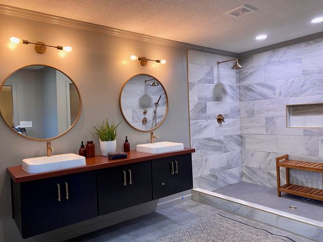 Modern bathroom with floating vanity, round mirrors, marble shower, and bronze fixtures.