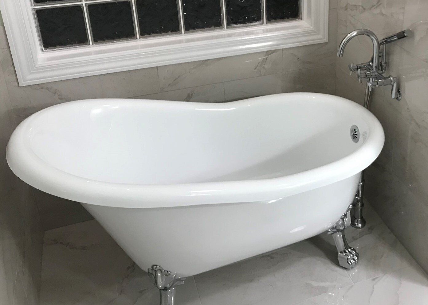 White clawfoot bathtub with chrome fixtures near a window in a bathroom.