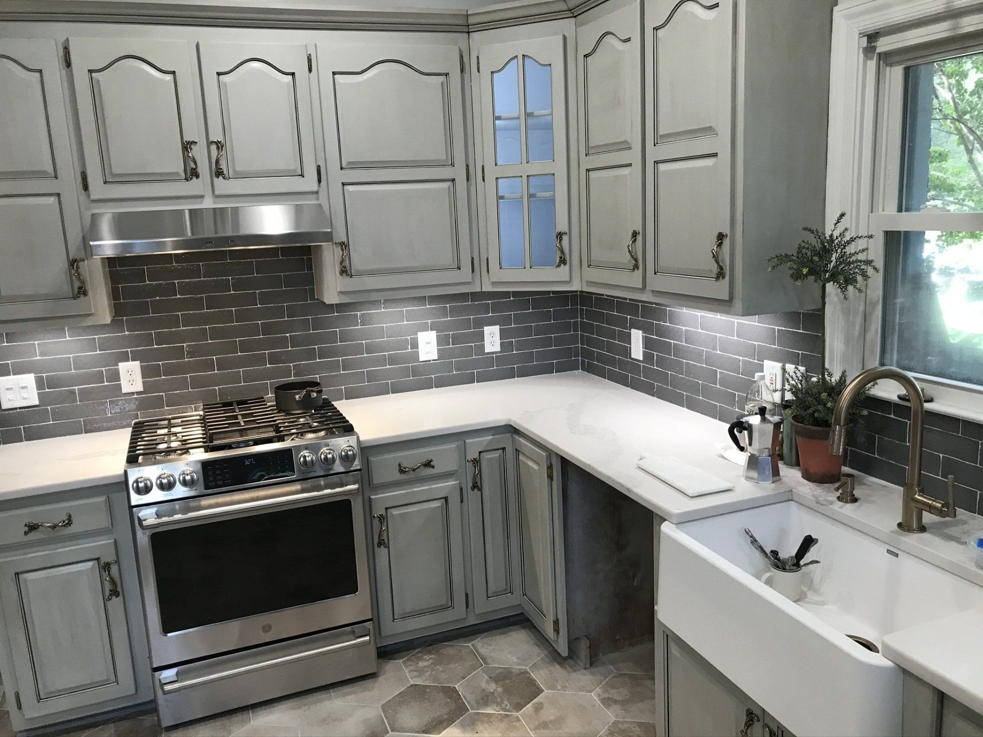 Gray and white kitchen with stainless steel appliances, tile backsplash, and farmhouse sink.