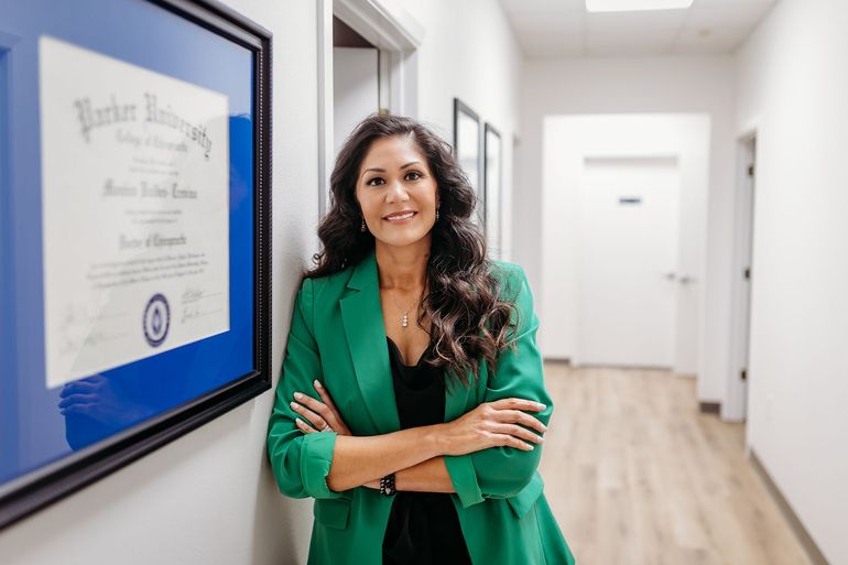 Woman in green blazer standing in a bright hallway beside a framed diploma