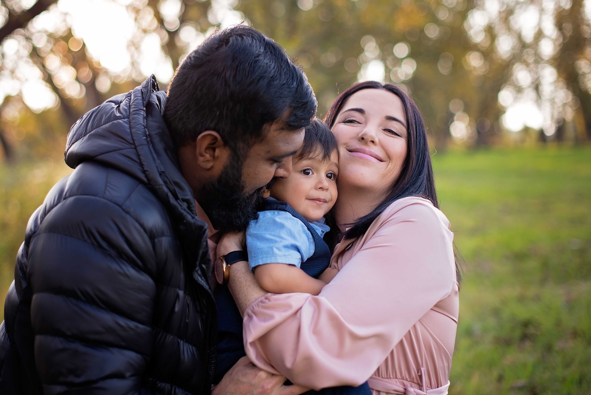 A man and a woman are holding a baby in a park.