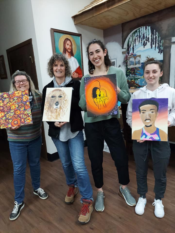 A group of people are standing next to each other holding paintings.