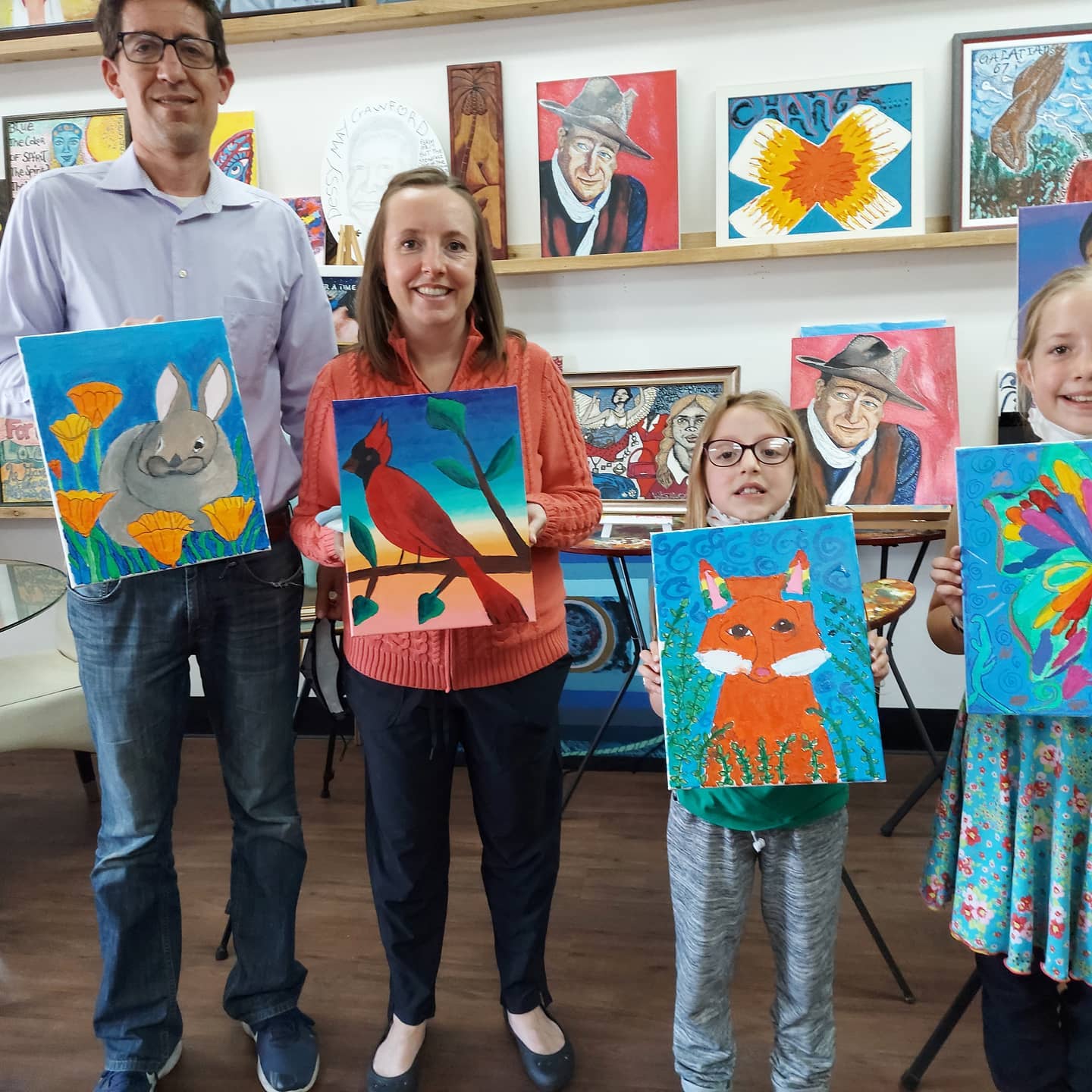 A group of people holding up paintings of animals and birds