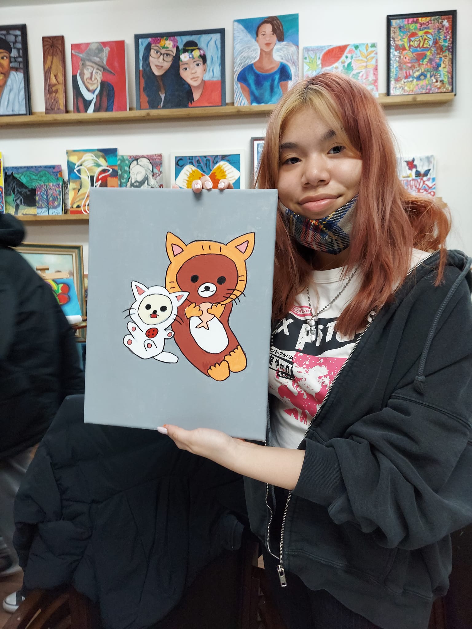 A woman is holding a painting of two cats and a bear.