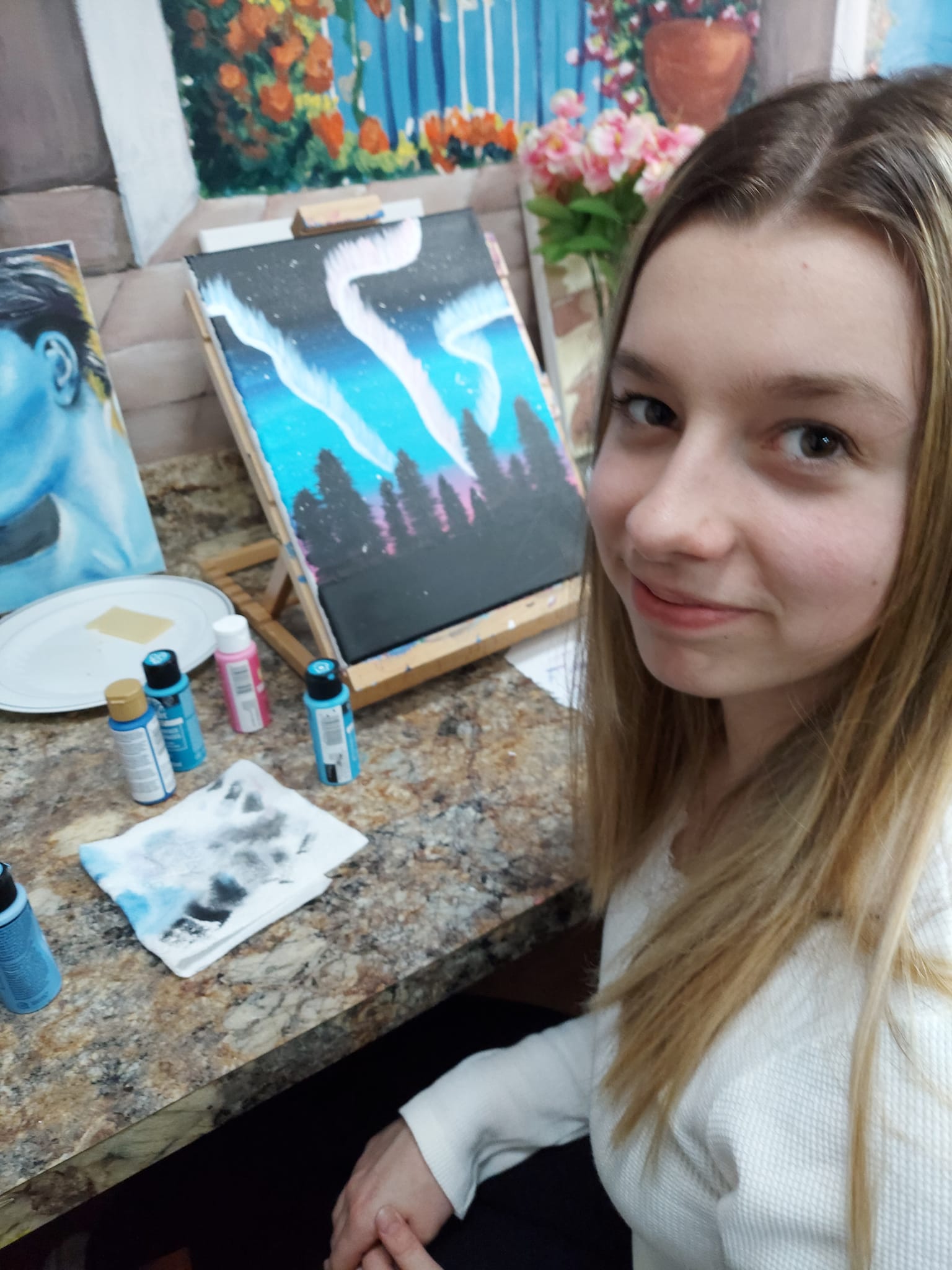 A young girl is sitting at a table with a painting on it.