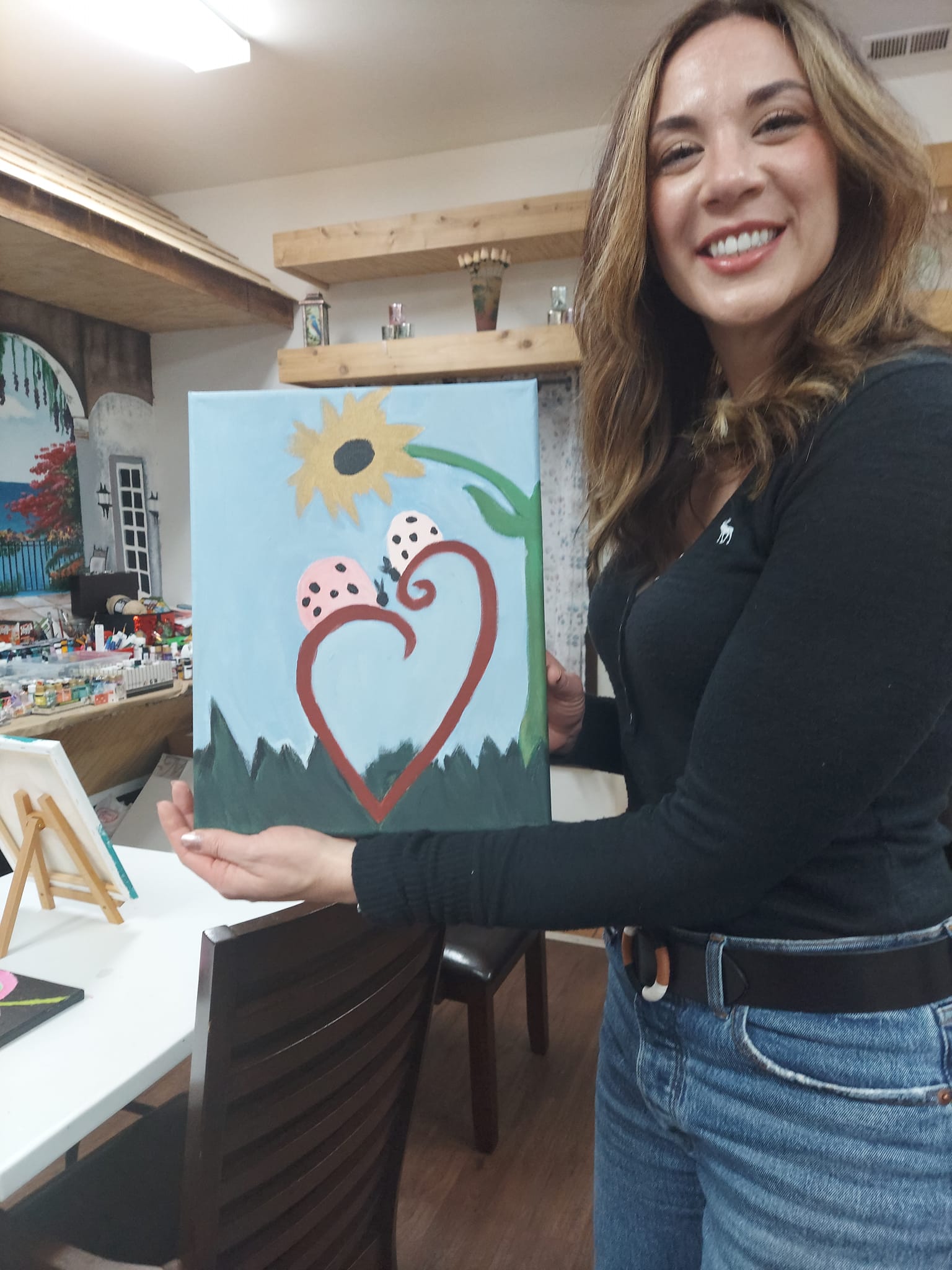 A woman is holding a painting of a heart with ladybugs on it.