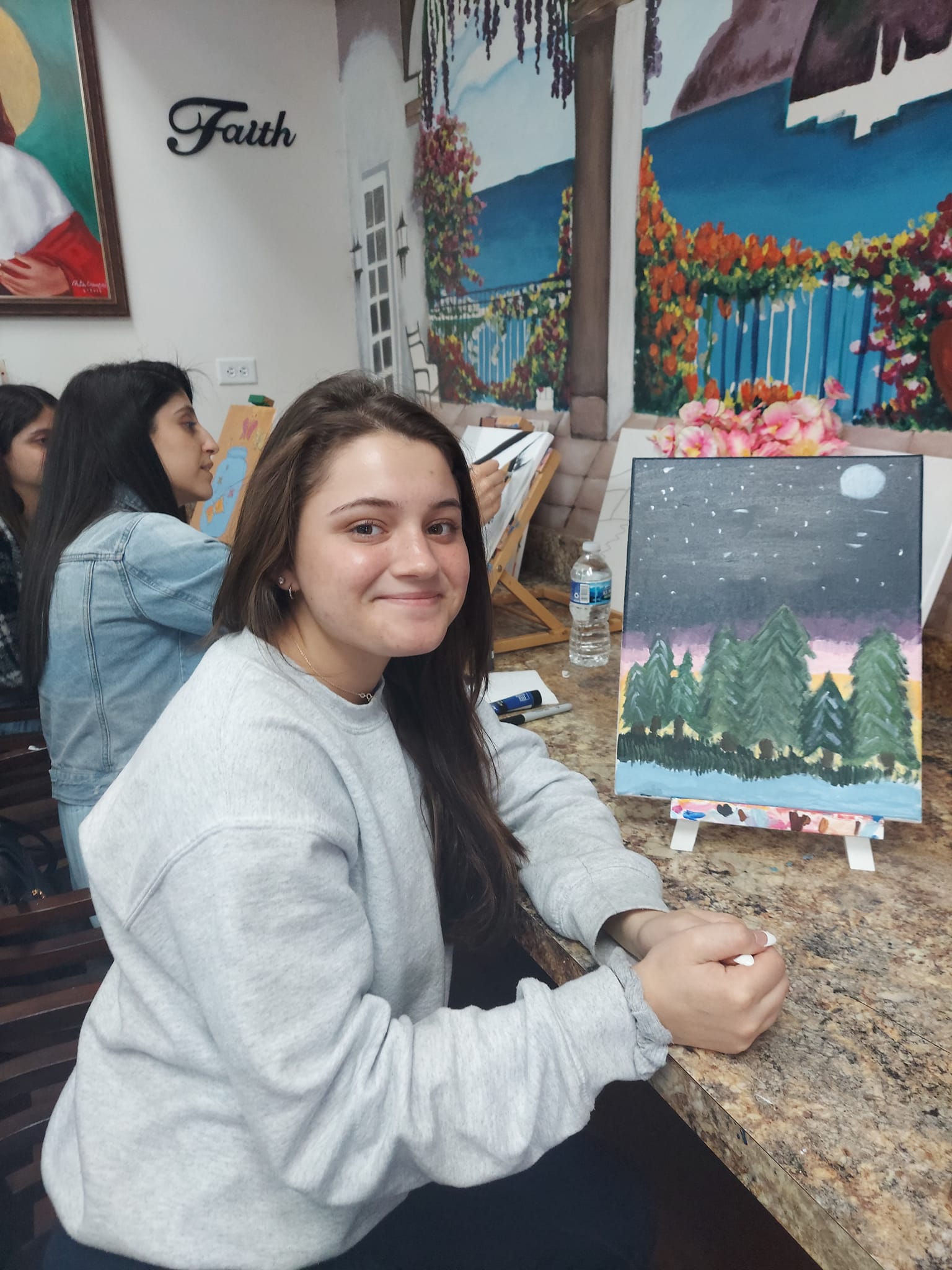 A woman is sitting at a table with a painting on it.