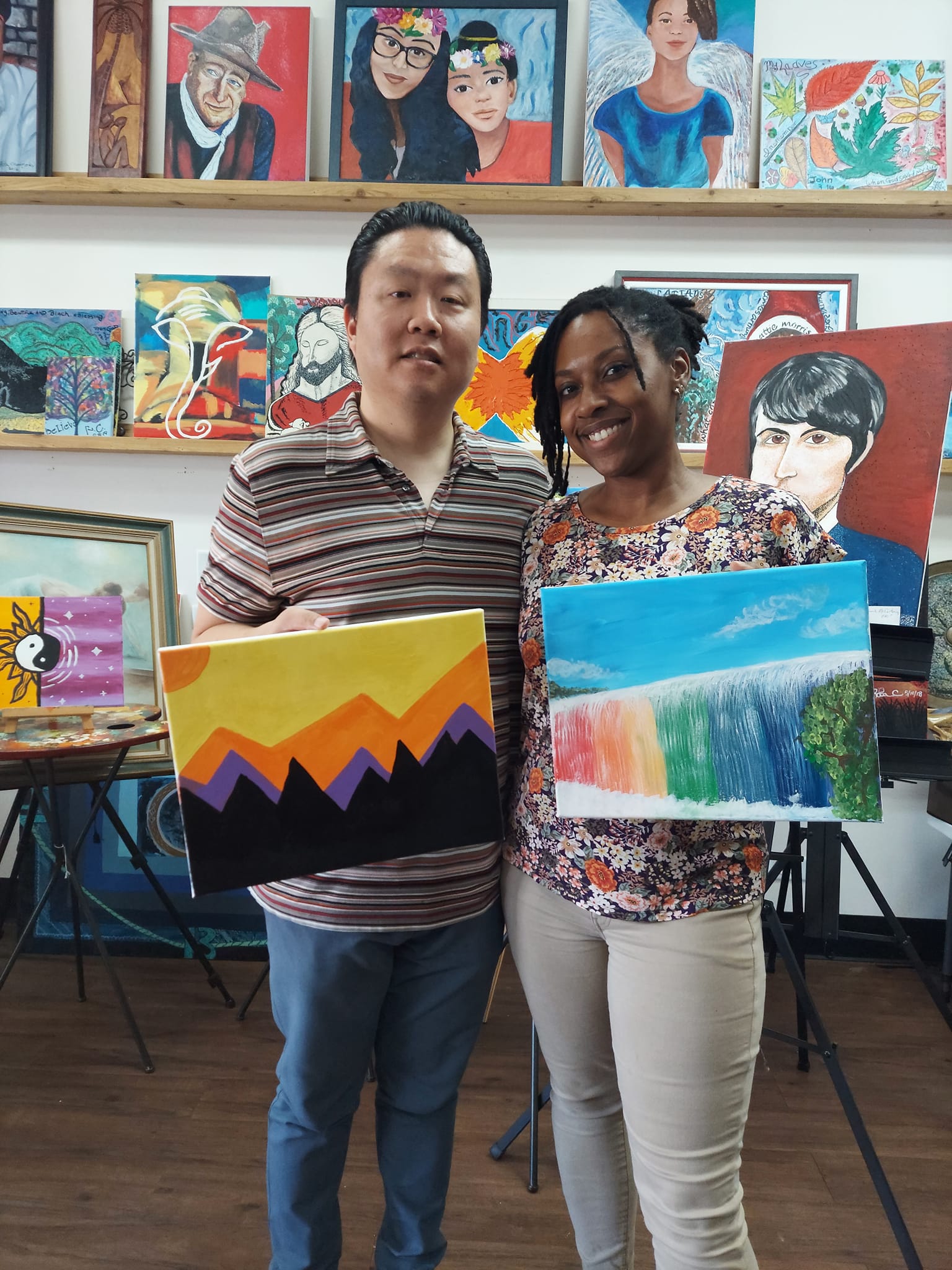 A man and a woman are standing next to each other holding paintings.