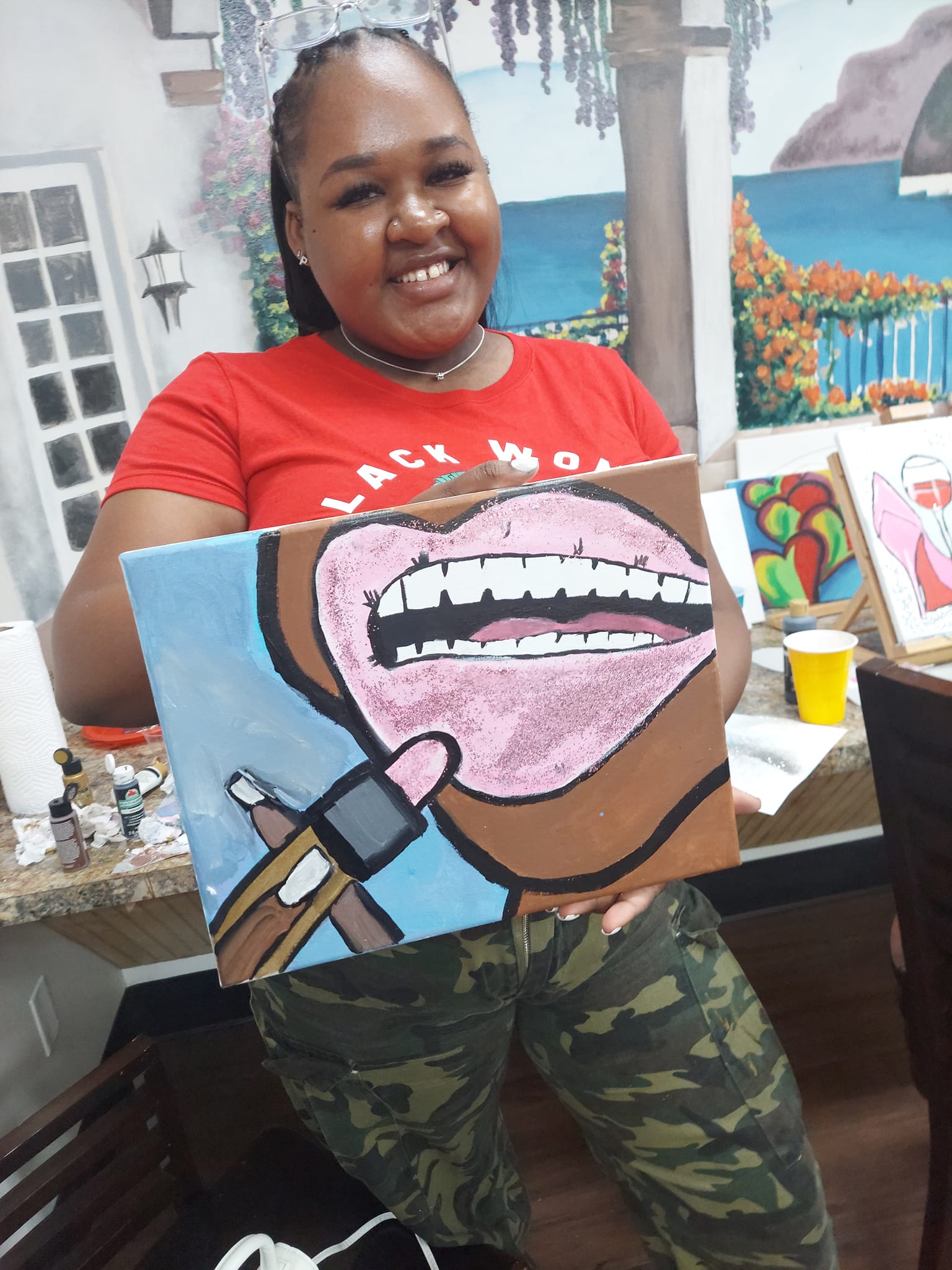 A woman is holding a painting of a woman 's mouth with lipstick on it.