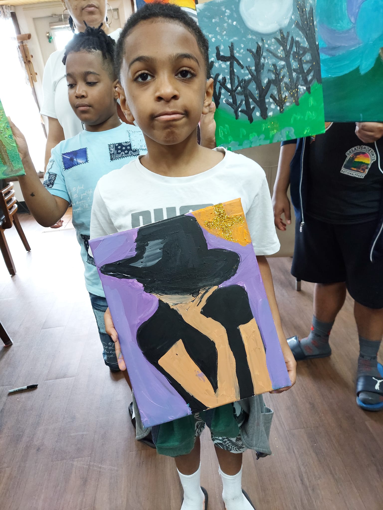 A young boy is holding a painting of a man in a hat