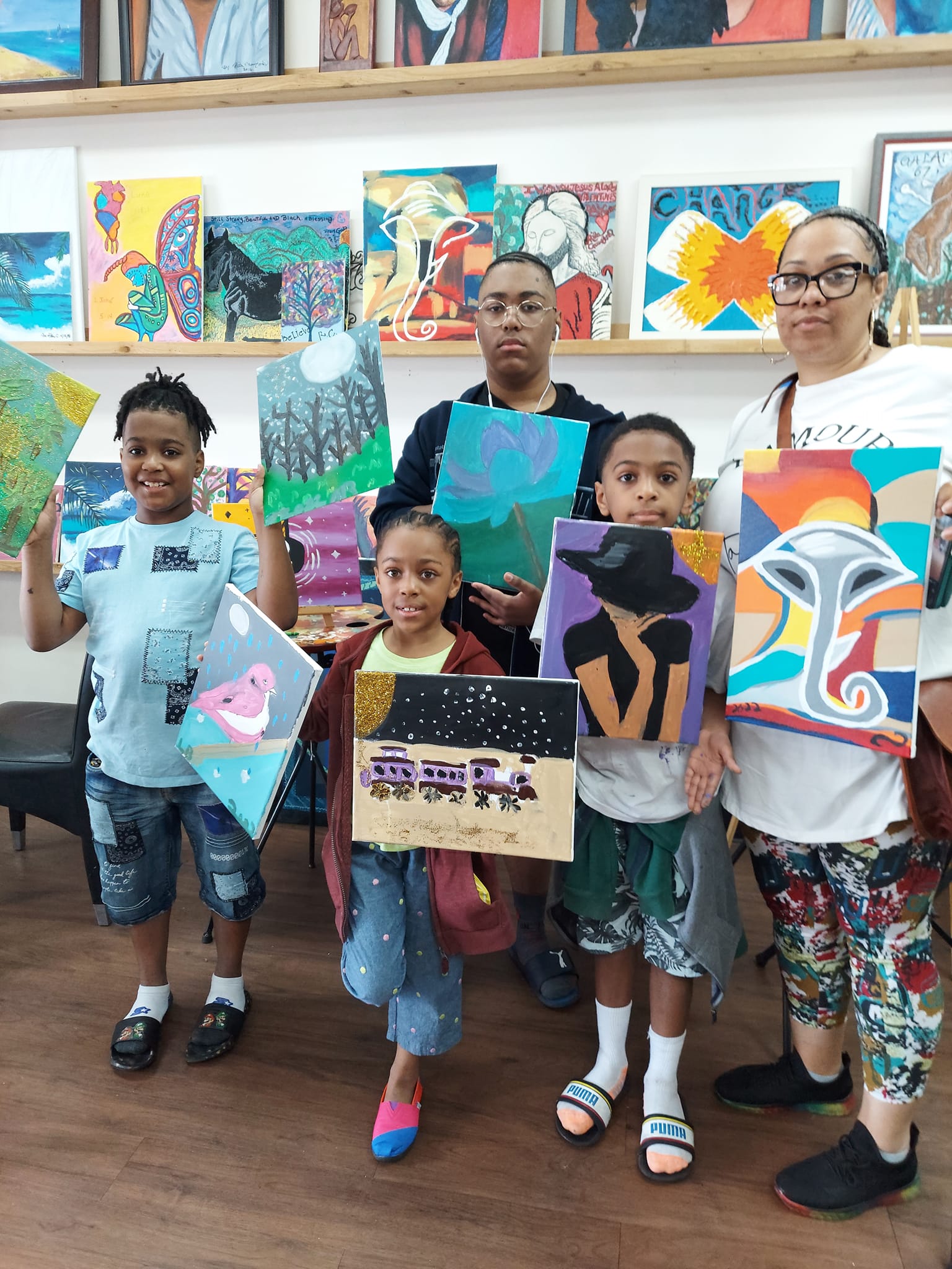 A group of children are holding up their paintings in a room.