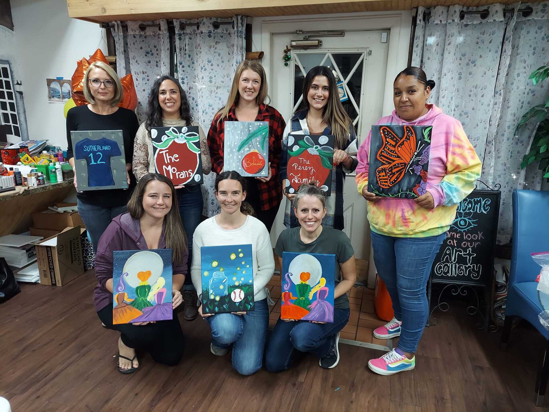 A group of women are posing for a picture with their paintings.