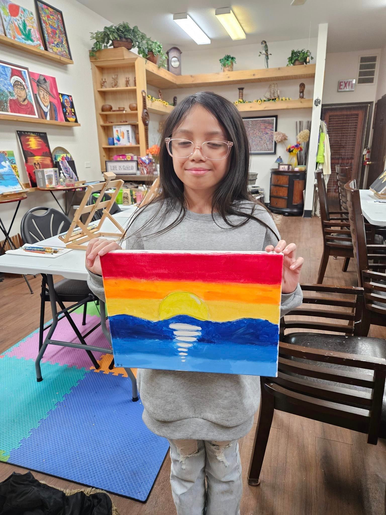 A young girl is holding a painting of a sunset in a room.