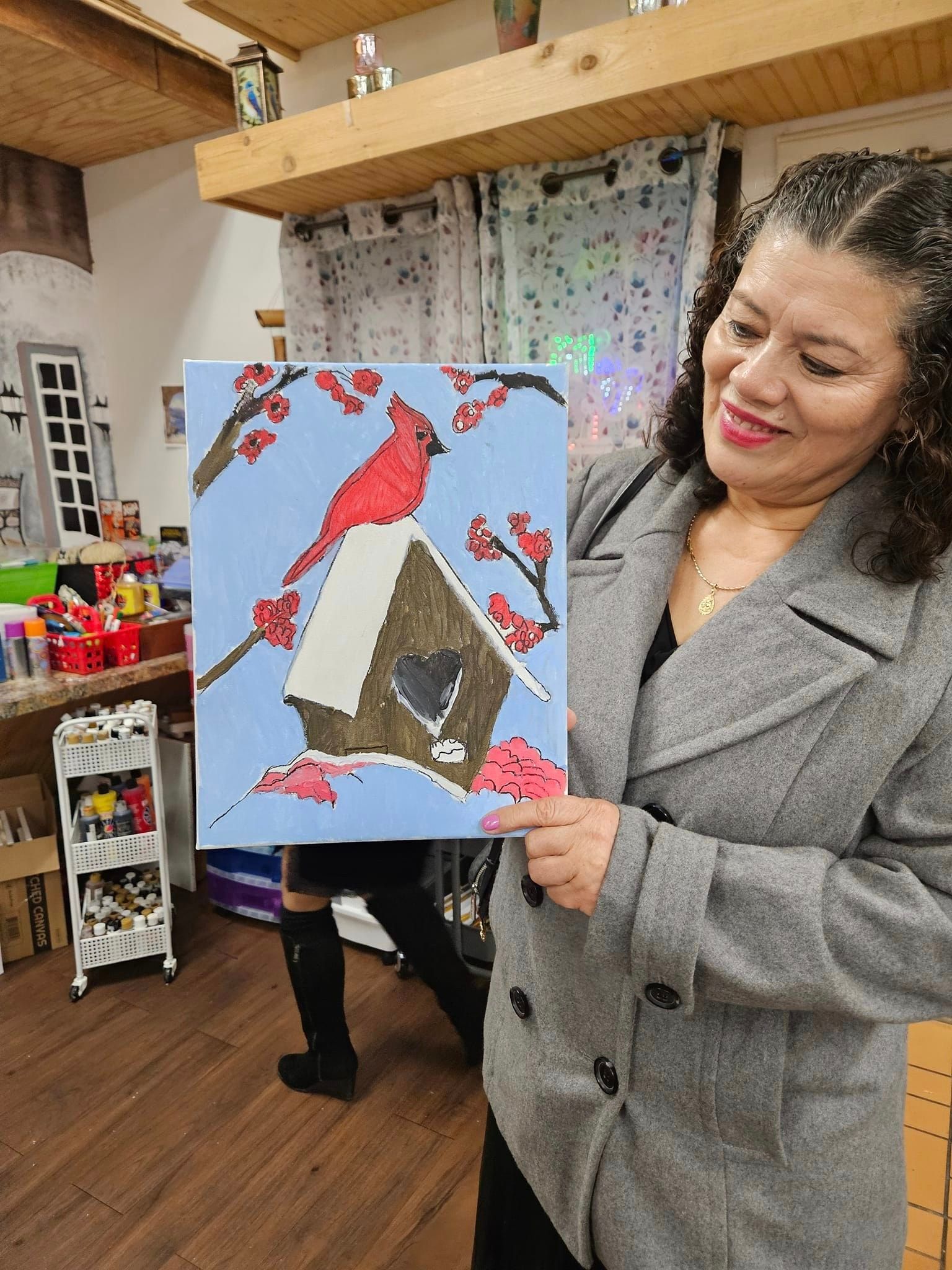 A woman is holding a painting of two cardinals in a birdhouse.