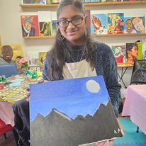 A young woman is holding a painting of mountains and a moon.