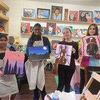 A group of women are holding paintings in a room.